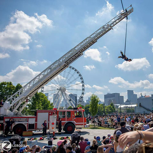 Camion de pompiers avec un pompier qui fait des acrobaties suspendu à l'échelle.